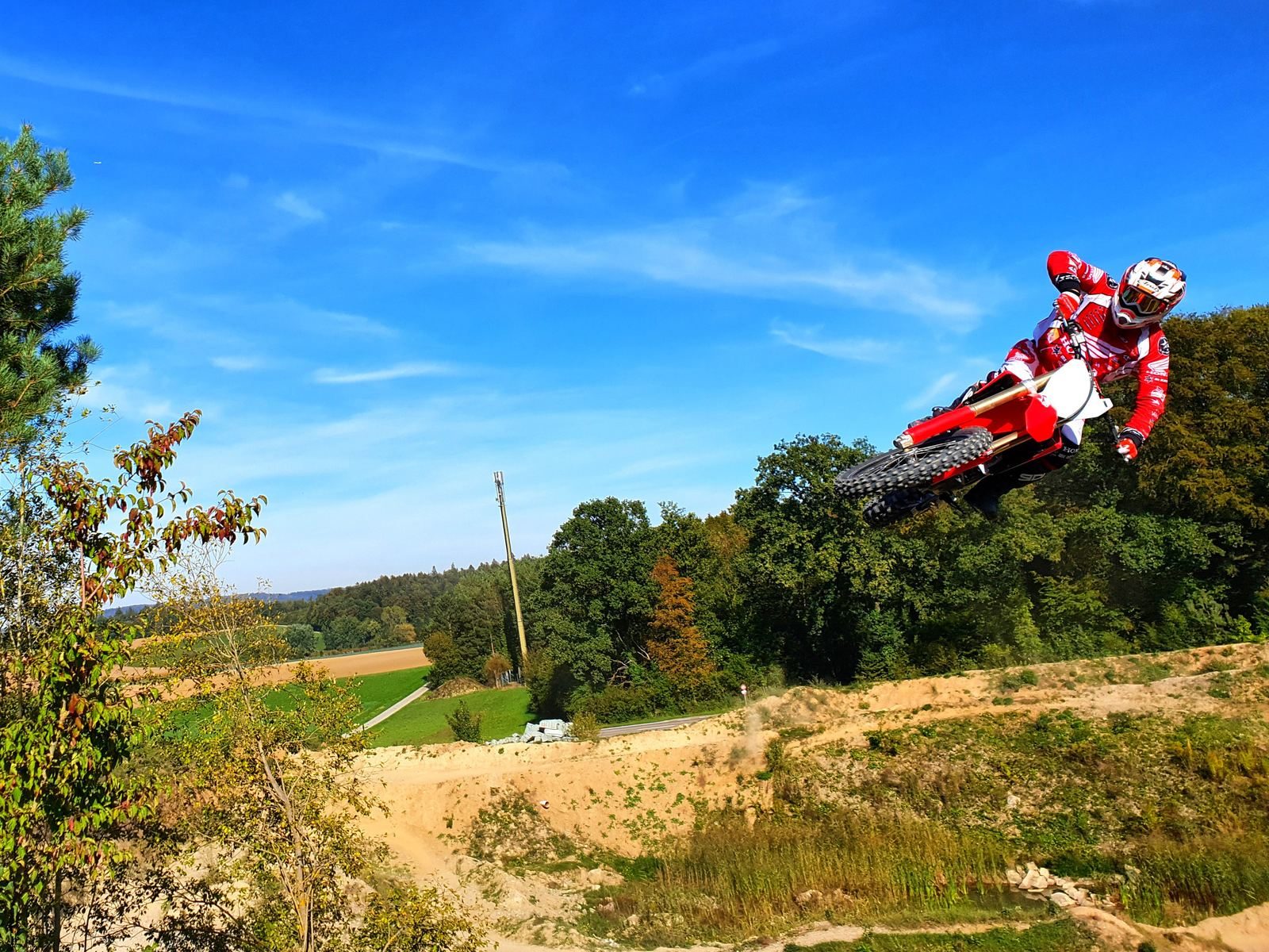Motocross Schule MX-Academy: Fahrer im Sprung vor blauem Himmel über grüner Landschaft